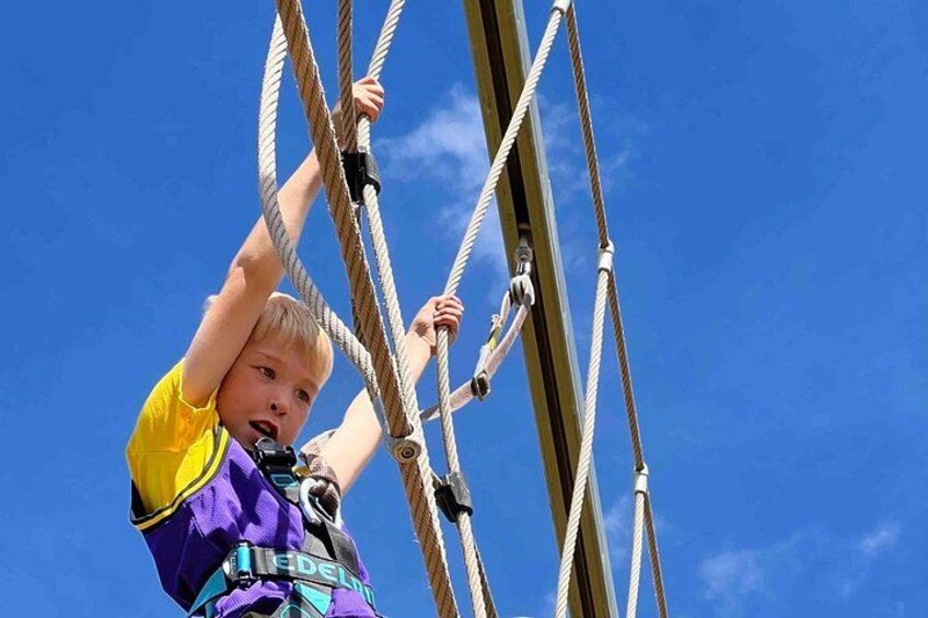 A person climbing a rope structure against a clear blue sky. 3