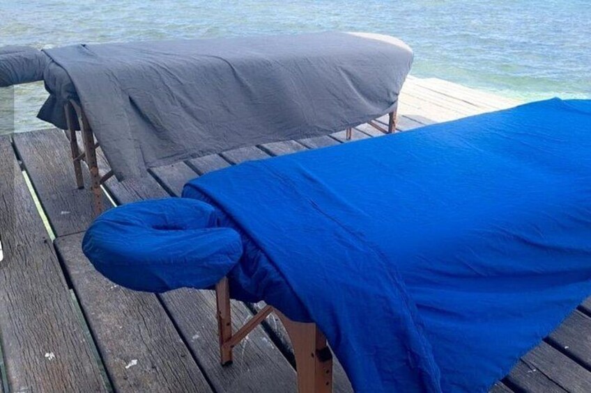 A wooden deck with two massage tables covered with blue and gray sheets. 3
