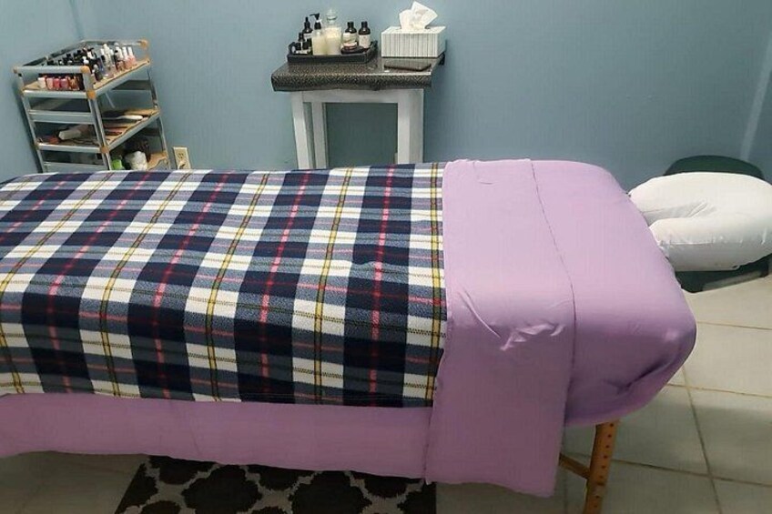 A bed with a plaid bedspread and a white pillow in a room with a blue wall and a small table with bottles. 5