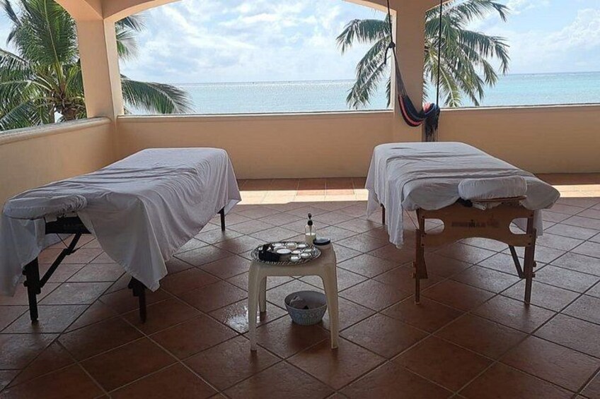 Two massage tables with white sheets, a small stool with a bowl, and a hammock. 1