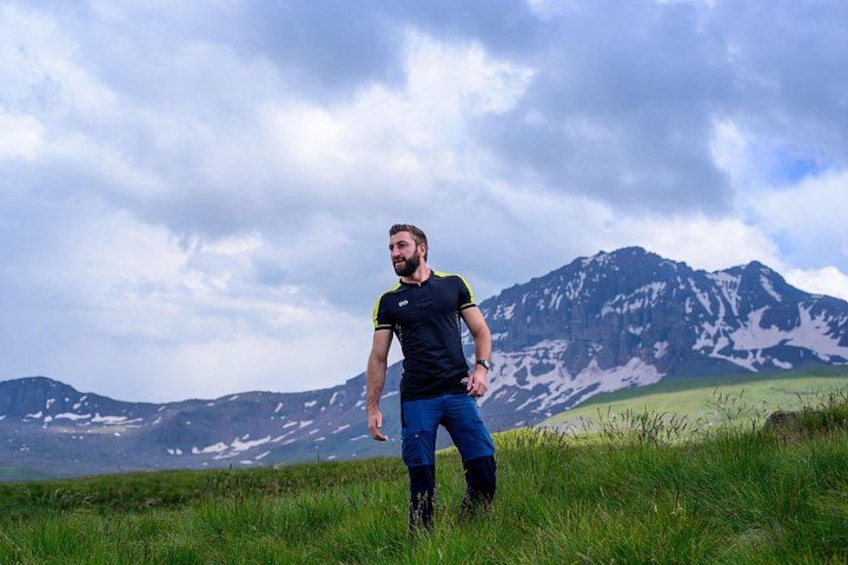 A person standing in a grassy field with mountains in the background. 2