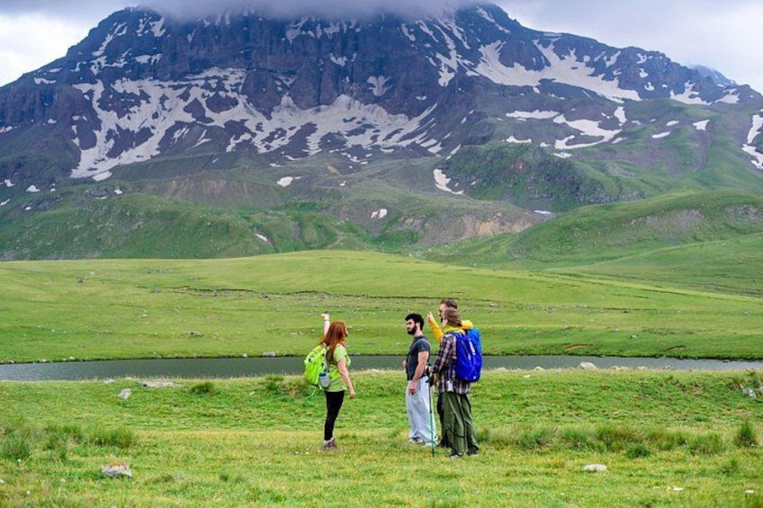 A group of people standing in a grassy field with a mountain in the background. 1