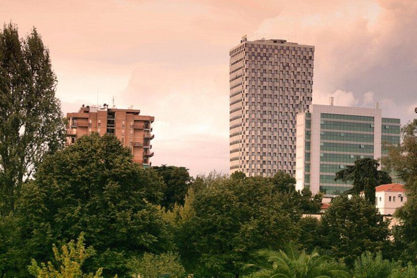 Stadsgezicht met moderne gebouwen, weelderige begroeiing en een bewolkte lucht. 3