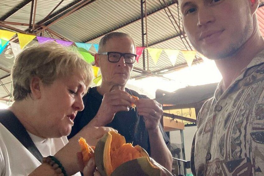 Three people eating at a food stall with colorful flags in the background. 3