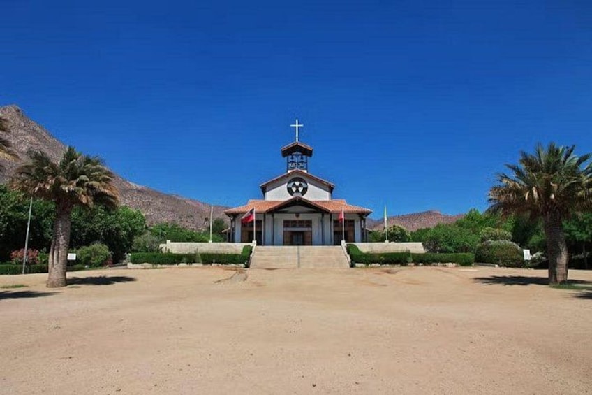 Una iglesia con una cruz en la parte superior, rodeada de palmeras y un cielo azul despejado. 3