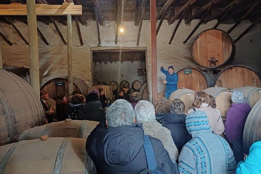 Un grupo de personas en un sótano rústico con barriles de madera y alguien dando una presentación. 5