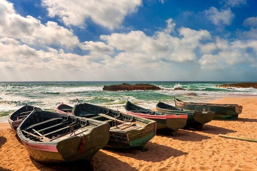 A beach with several boats lined up on the sand, the ocean in the background, and a rocky outcrop in the distance. 4