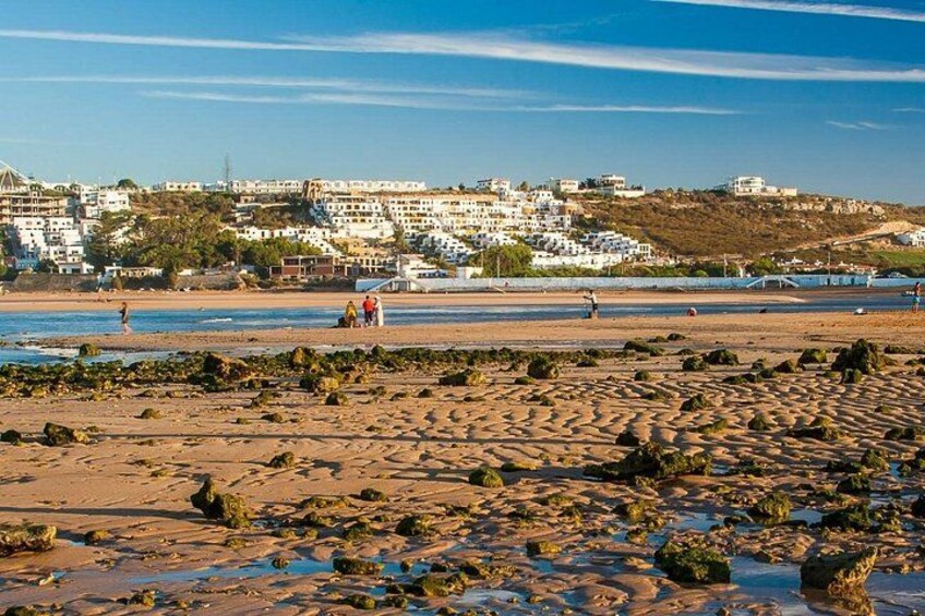 A beach with rocky terrain, a coastal town in the background, and a clear sky. 5