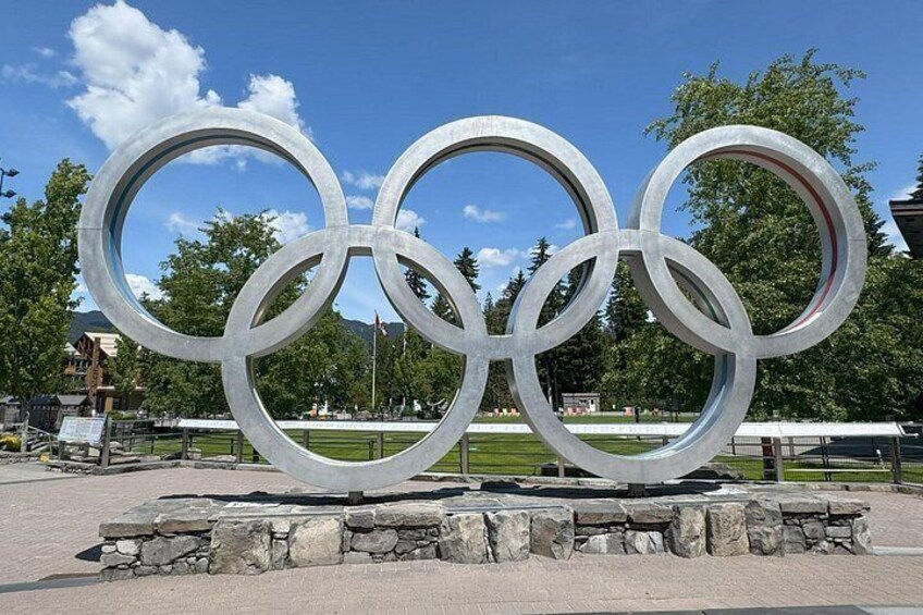 Una gran escultura de los anillos olímpicos en un espacio abierto con árboles y un cielo despejado al fondo. 3