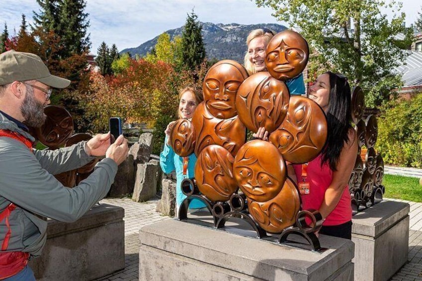 Un grupo de personas tomando una foto con una escultura de rostros. 5