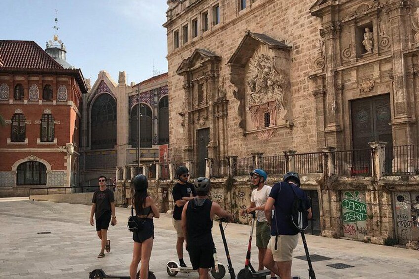 Een groep mensen met scooters voor een historisch gebouw met rijke architectuur. 2