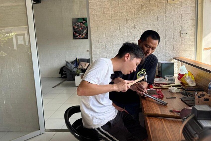 Twee personen werken aan een houten tafel, met gereedschap en een laptop. 3