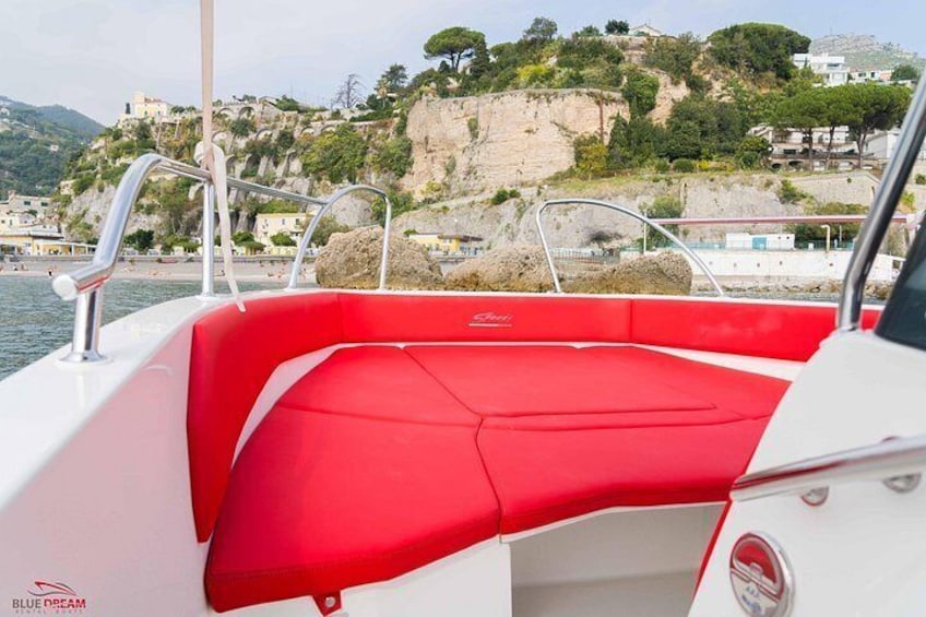 A boat with a red interior, a rocky coastline, and buildings in the background. 3