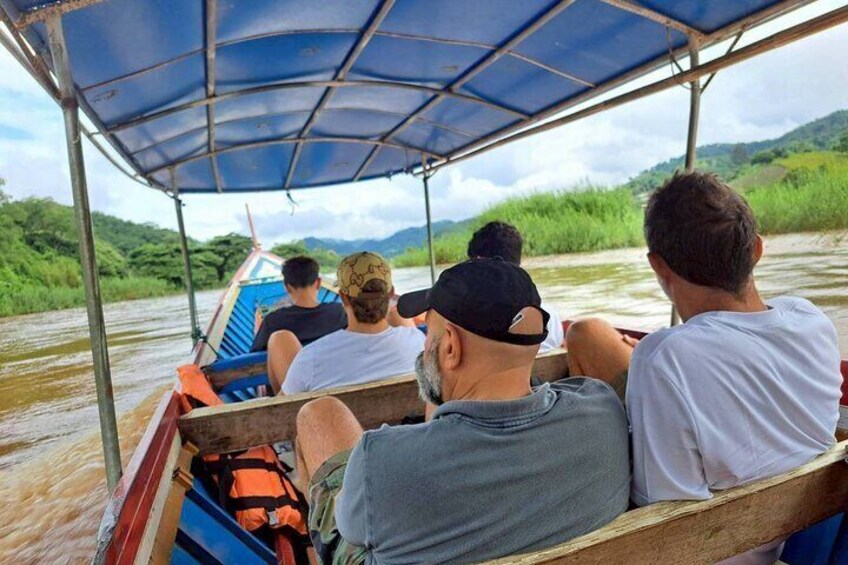 Menschen in einem Boot unter einem blauen Verdeck, umgeben von Grünpflanzen und Wasser. 1