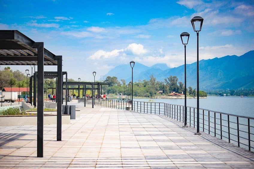 A waterfront promenade with a covered seating area, lamp posts, and a view of mountains. 4