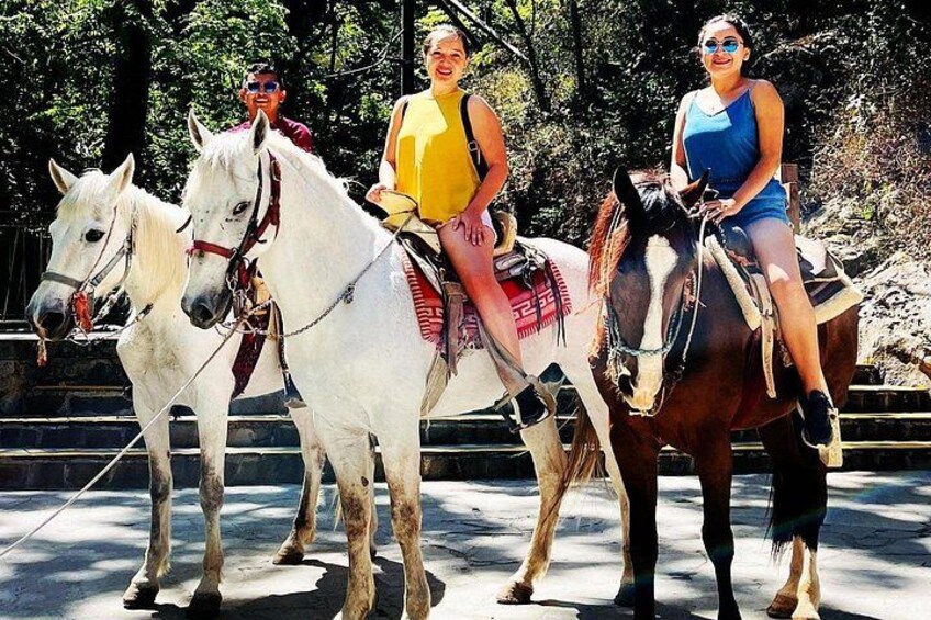 Three people riding horses on a paved path with trees in the background. 1