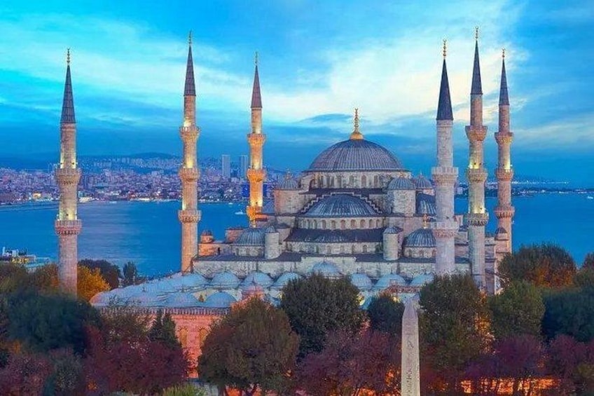 A large mosque with multiple minarets and a dome, surrounded by trees and overlooking a body of water. 2