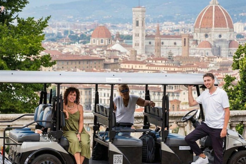 A golf cart with three people, a cityscape with prominent domed buildings in the background. 1