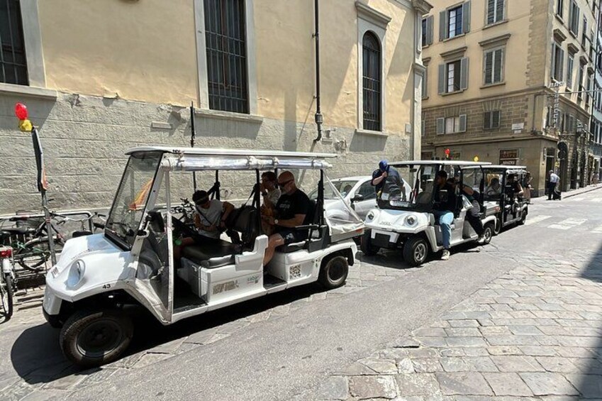 A row of golf carts on a cobblestone street with tourists. 3
