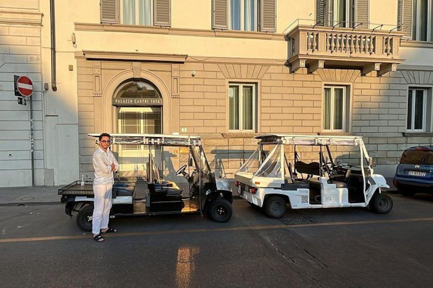 A person standing next to a white utility vehicle on a street with a building in the background. 2