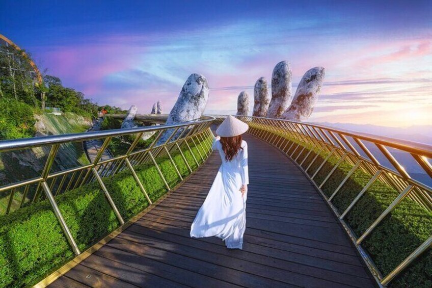 A woman in a white dress walking on a wooden boardwalk with a railing, surrounded by greenery and large rock formations. 3