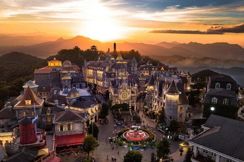 A castle-like building complex with a central circular plaza, surrounded by smaller structures and a mountainous backdrop. 3