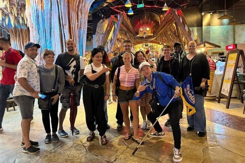 A group of people posing in a colorful indoor setting with hanging fabrics and a wooden structure in the background. 5