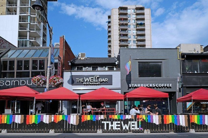El Well Bar y Starbucks Coffee con sombrillas rojas, una bandera arcoíris y una valla. 5