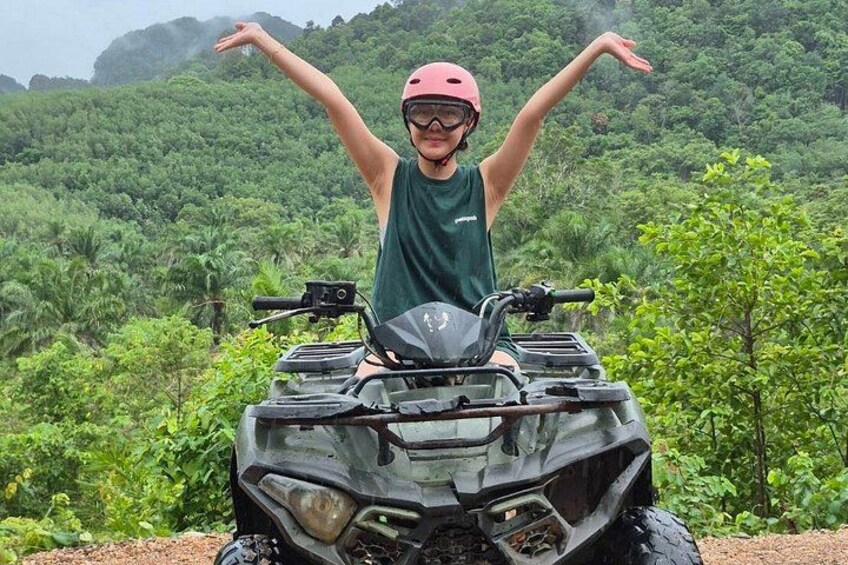A person on an ATV with arms raised, surrounded by dense green foliage. 3