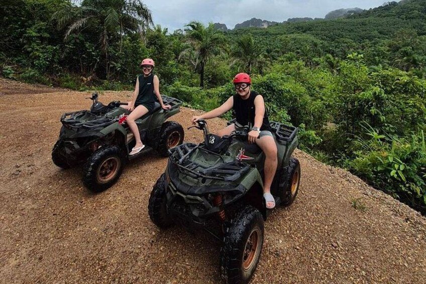 Two people on ATVs on a dirt path surrounded by greenery. 4