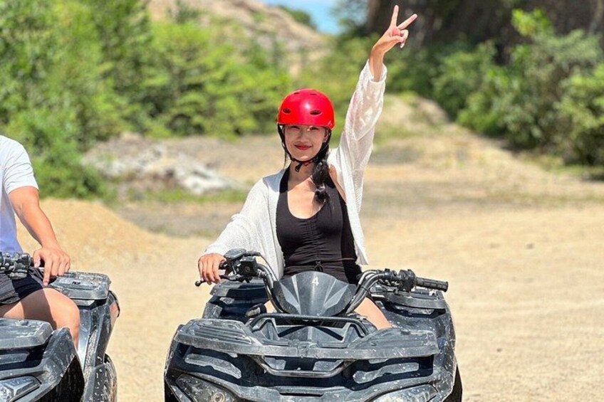 Two people on all-terrain vehicles (ATVs) in a natural setting with greenery and rocky terrain. 1