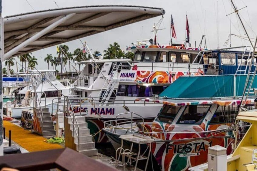 A marina with boats docked, including a colorful boat with 'MIAMI' and 'FIESTA' written on it. 2