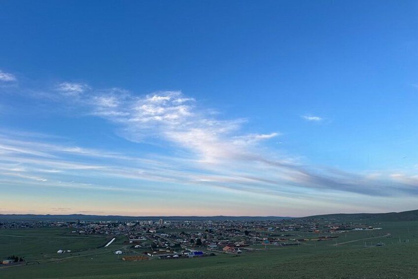 A wide landscape with a clear sky, a distant town, and a green field. 5