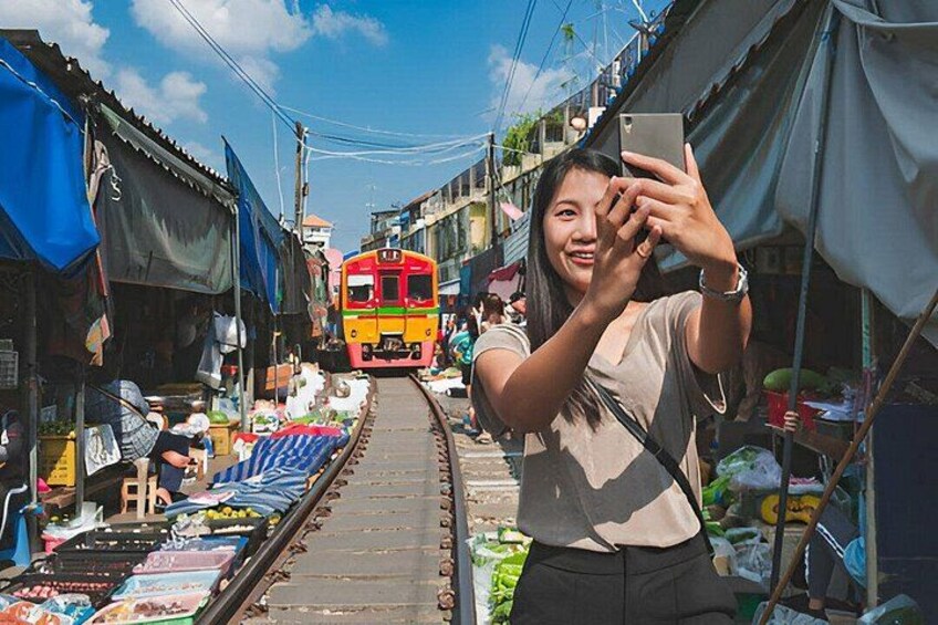 En smal gade med et tog i baggrunden, markedsboder langs begge sider og en person der tager en selfie. 1