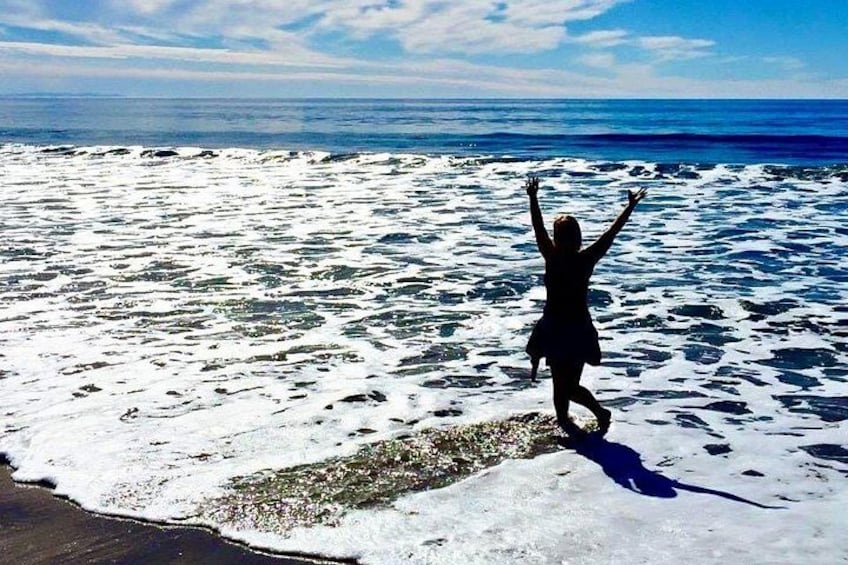 A person standing on a beach with arms raised, facing the ocean. 2