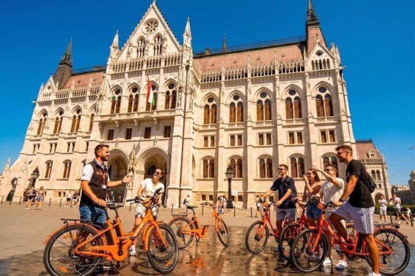 Un edificio storico con architettura elaborata, un gruppo di persone in bicicletta e un cielo azzurro limpido. 1
