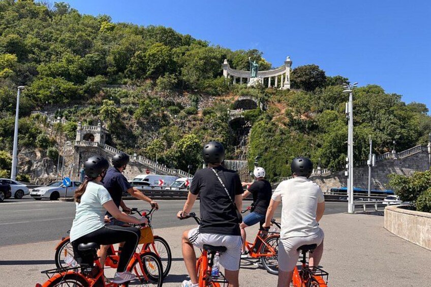 A group of cyclists on a paved path with a hilly landscape and a temple in the background. 3