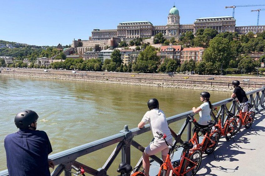 A river with a bridge, cyclists, and a historic building in the background. 2