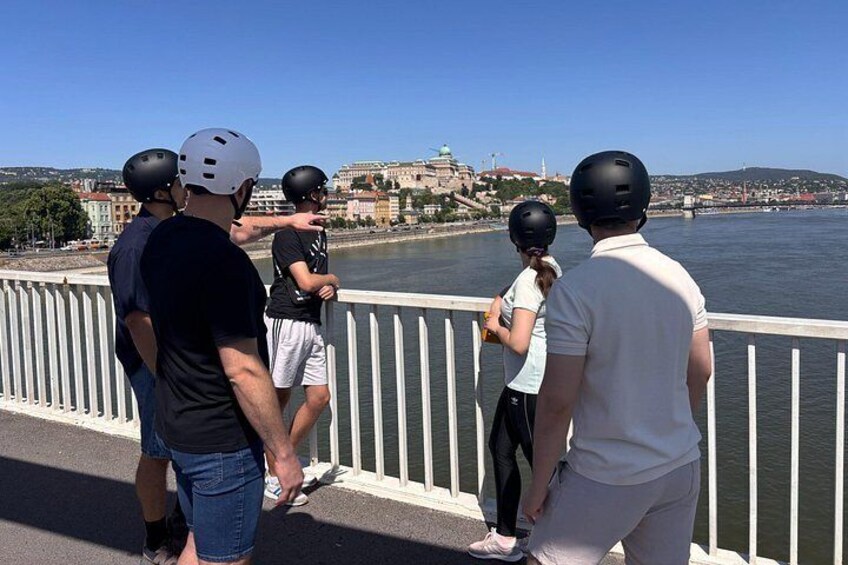 A group of people on a bridge with a river and buildings in the background. 2