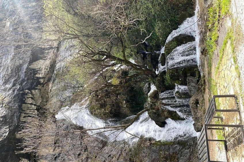 A waterfall cascading down a rocky cliff, surrounded by trees and a wooden viewing platform. 2