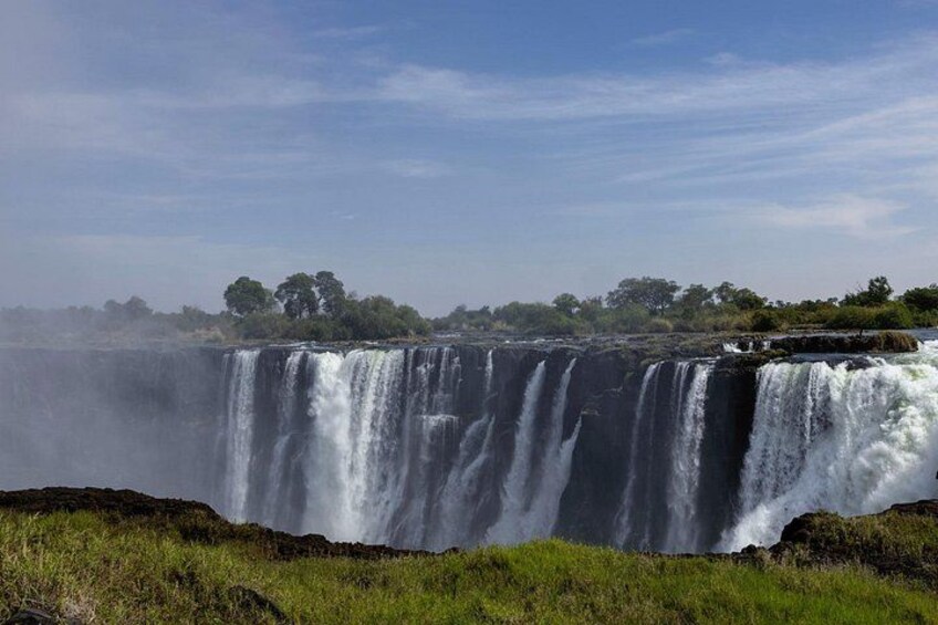 A large waterfall with multiple cascades, surrounded by grassy terrain and trees in the background. 5