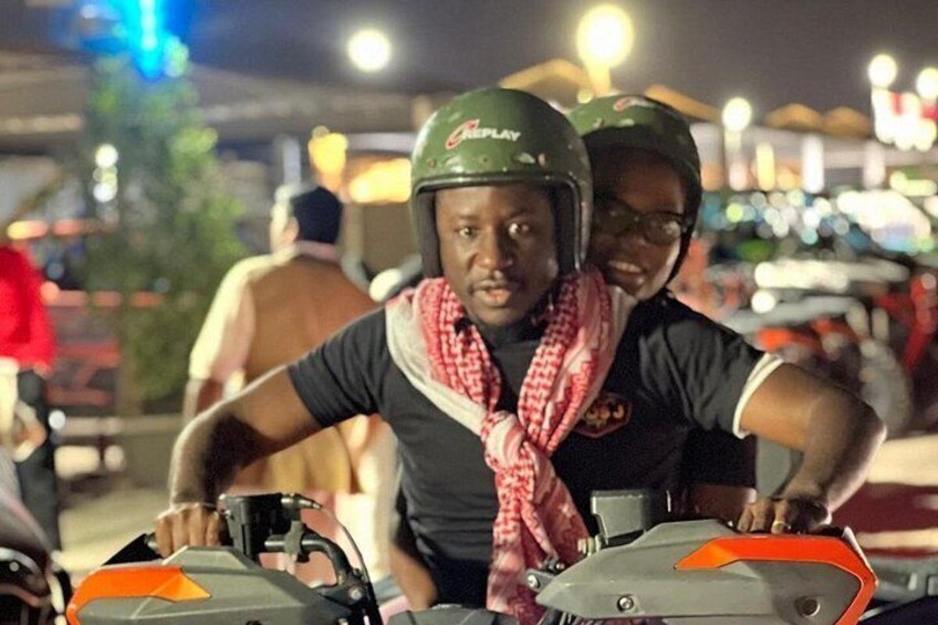 Two individuals on a motorcycle, wearing helmets and a scarf, in an urban setting at night. 3