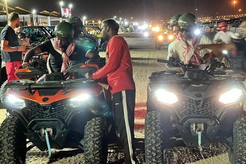 People on ATVs, a dirt road, and vehicles in the background. 2