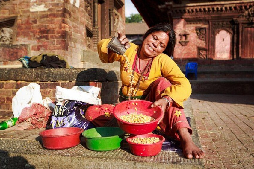 A person sitting on the ground, pouring grains from a bag into a red bowl. 2