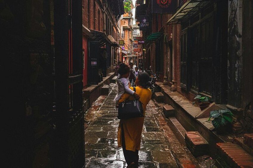 A narrow alley with wet cobblestone pavement, brick buildings, and a few pedestrians. 4