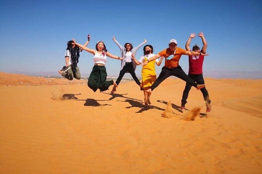 A group of people jumping in a desert with sand dunes in the background. 2