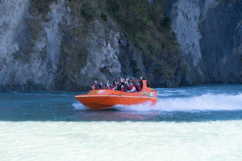 Una lancha roja con pasajeros navegando por aguas azules cristalinas, con un acantilado rocoso al fondo. 3