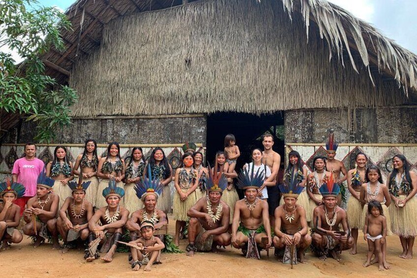 Un groupe de personnes, vêtues de costumes traditionnels, posent devant une hutte à toit de chaume. 3
