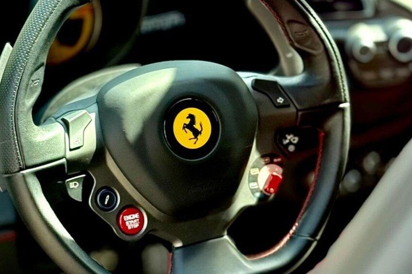 Een stuurwiel van een Ferrari met het bekende logo, een versnellingspook en een cruise control knop. 4