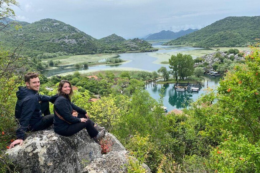 Un couple est assis sur un rocher, d’où il jouit d’une vue sur un lac entouré de verdure et de collines. 4